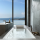 Baño de hotel con bañera y lavabo junto a ventanal con vista al mar