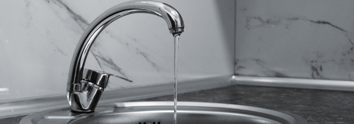Grifo cromado con agua corriendo sobre fregadero, azulejo de mármol