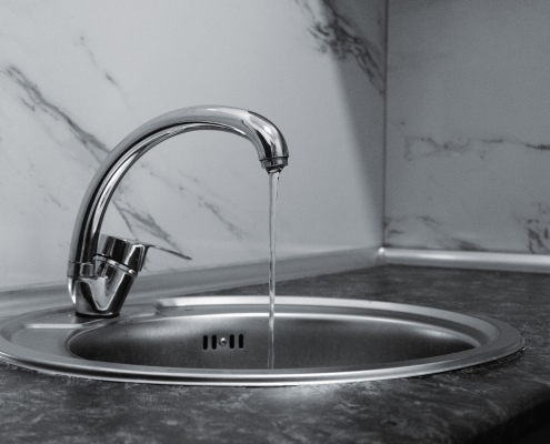 Grifo cromado con agua corriendo sobre fregadero, azulejo de mármol