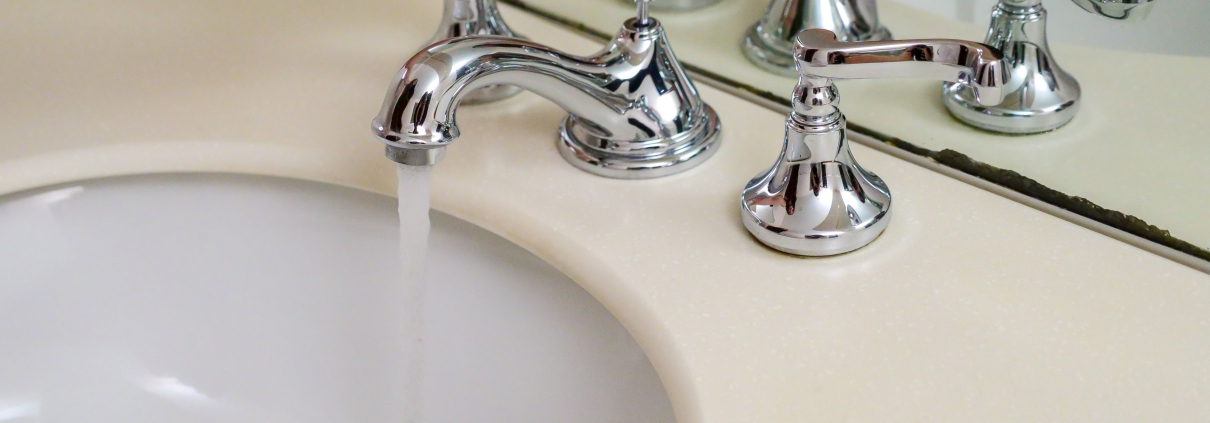 Mano abriendo un grifo cromado clásico con agua corriendo sobre un lavabo