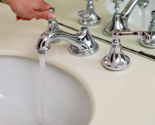 Mano abriendo un grifo cromado clásico con agua corriendo sobre un lavabo