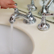 Mano abriendo un grifo cromado clásico con agua corriendo sobre un lavabo